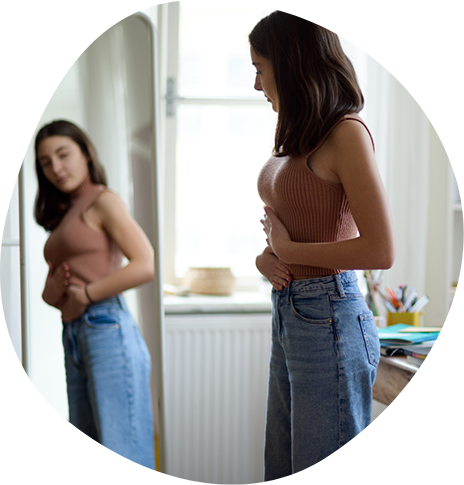 Thin woman looking at the size of her stomach in a mirror